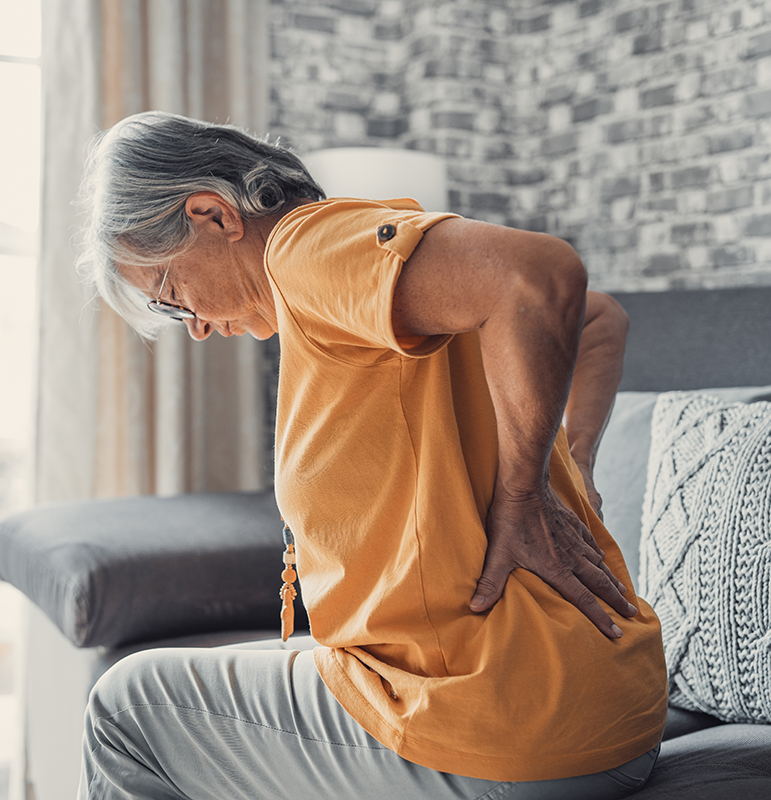 Unhappy mature woman touching back, feeling pain, sitting on couch in living room, unhealthy middle aged senior female suffering from backache, spinal problem, rubbing stiff muscles or kidney